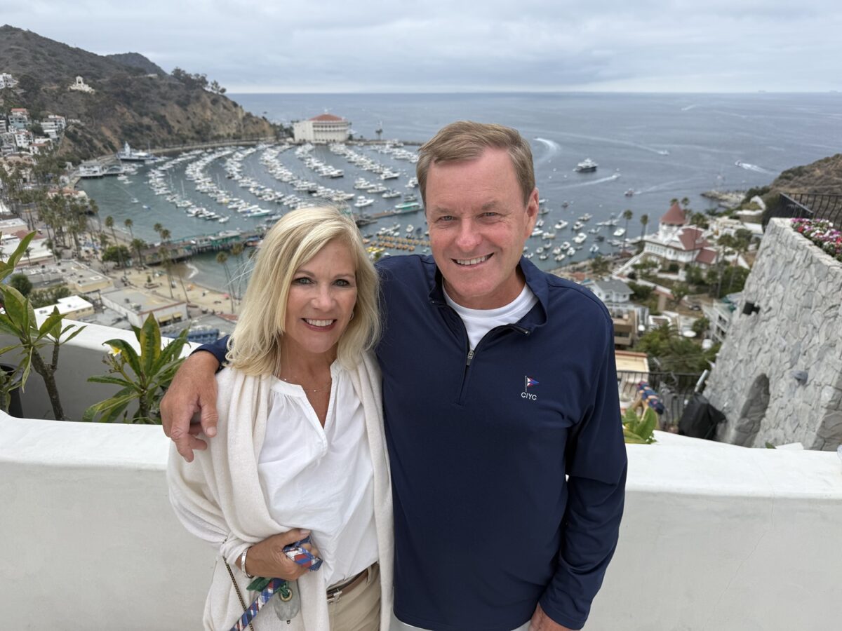 Devin Doyle and his wife posing together with a harbor and marina overlooking the ocean.