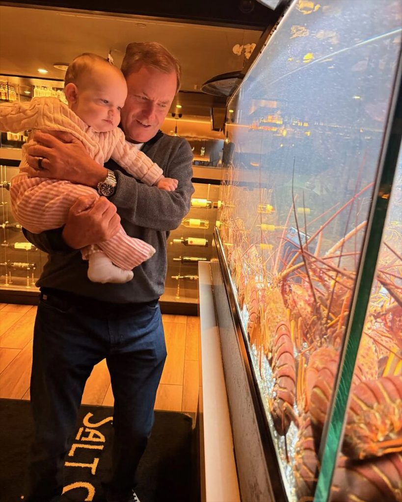 Devin Doyle holding a baby while looking at a large aquarium display filled with marine life.